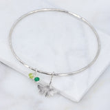 lightly hammered silver bangle with ginkgo charm and 3 green gemstones on a marble tile 