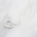 A silver hammered hoop pendant with tiny bobbles on a delicate chain against a white marble background.